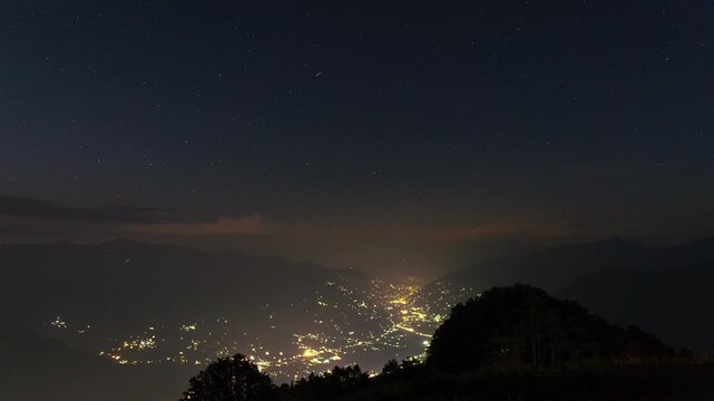 4K Night Timelapse of stars moving in sky above Kullu Valley as seen from Mahili Thatch campsite, Himachal Pradesh, India. Nightlapse of stars moving above glowing city lights and Himalayan mountains.