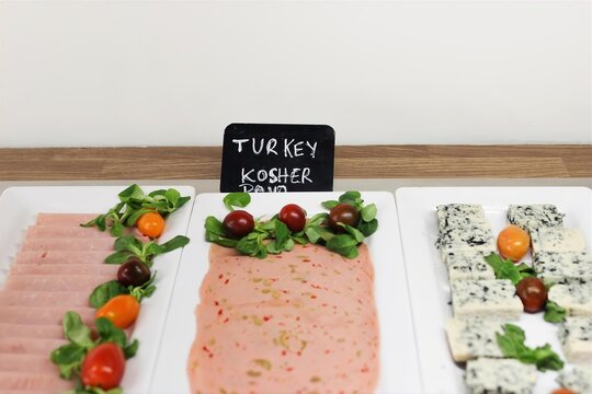 Kosher Turkey Ham Cold Cuts and Blue Cheese Breakfast Buffet. Fresh Greens, Cherry Tomatoes on White Platters. Hotel Catering, Brunch, Gourmet Deli and Hospitality Food Service. Blurred foreground