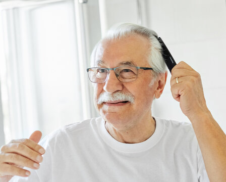 Portrait of an elderly senior man grooming and combing his hair in front of  mirror in bathroom