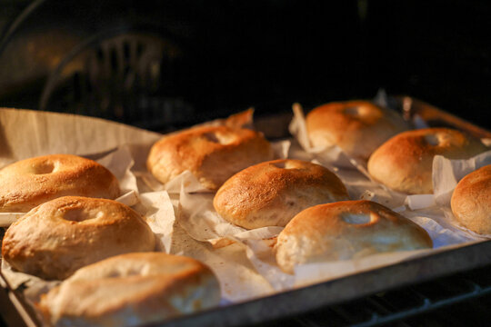 Homemade bagels baking in an oven, featuring golden crusts, artisan craftsmanship, fresh bread, and warm bakery-style food preparation.