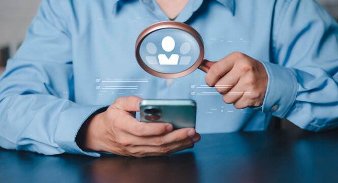 Hand using magnifying glass over user profile icons with checkmarks on smartphone. Professional recruitment screening, candidate vetting process, and target audience analytics concept for hiring.