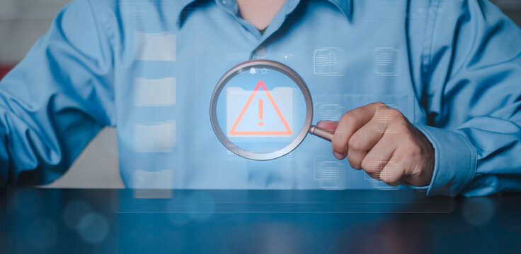 Cybersecurity audit, system vulnerability detection and information technology error inspection. Professional hand holding magnifying glass focusing on warning alert icon inside digital folder.