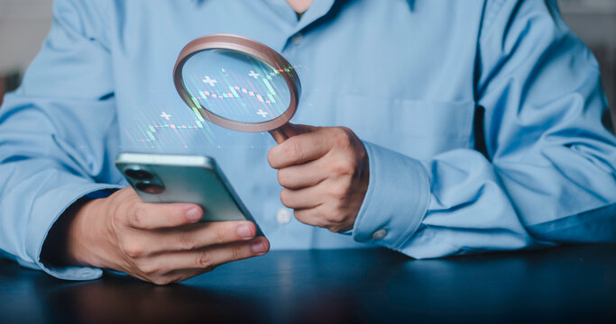 Investment strategy, profit research, and data analytics for trading success. Businessman using magnifying glass to analyze growing financial stock market chart on smartphone.