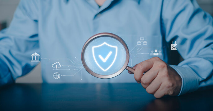 Security verification, quality assurance, system protection financial, privacy and certified data safety standards. Businessman holding magnifying glass focusing on glowing shield and checkmark icon