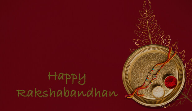 Traditional Raksha Bandhan thali with ornamental rakhi and gold foliage on maroon background.