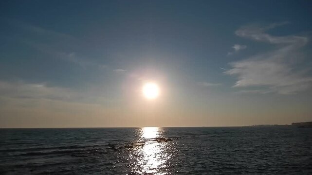 Calm water at sea, moving reflections of sun on small waves, blue sky with clouds on horizon and pathelione and two white lines from passing airplanes in parallel. Topics: travel, sea ​​view