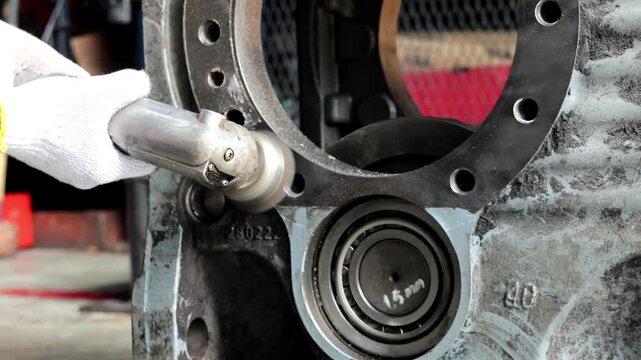 Worker using a power grinder tool to clean and finish the surface of a metal flange on an industrial machinery housing part.