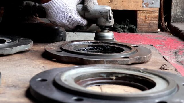 Worker using a power tool to grind and clean a metal flange surface during machinery repair in a workshop.