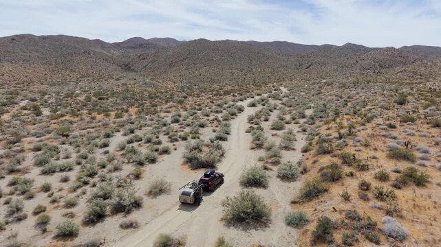 SUV drives with a teardrop camper trailer on dirt trails through Anza Borego desert mountains and hills in bright daylight.