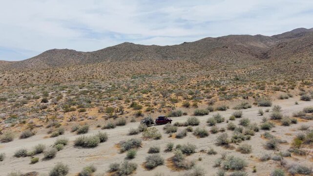 An suv pulls a teardrop camper trailer across dirt trails in the Anza Borego desert surrounded by mountains and hills