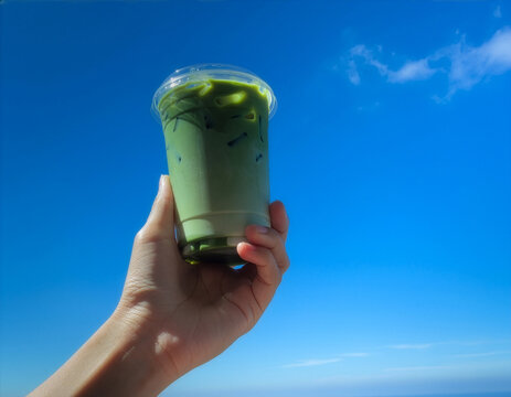 Iced matcha latte cup mockup template held by hand against blue sky