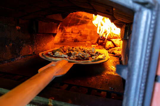 Chef placing raw pizza into a hot traditional wood-fired brick oven using a wooden peel