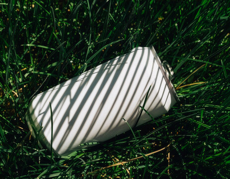 Blank white beer can mockup template lying in grass with striped shadows