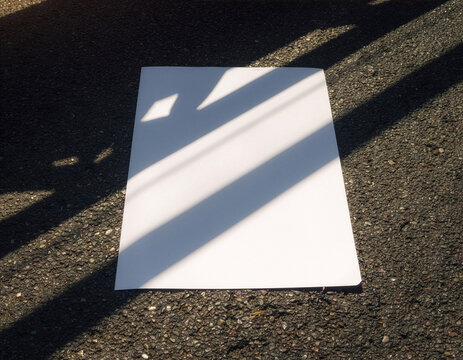 Blank white poster mockup template on asphalt with diagonal shadows