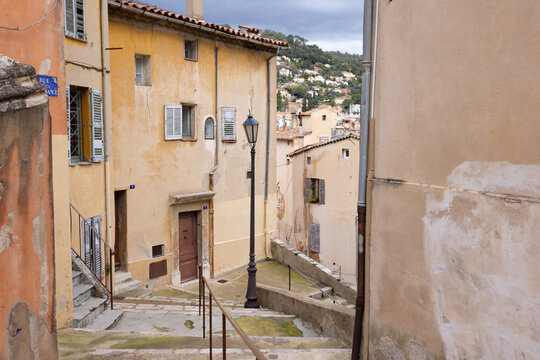 Stone steps wind down through the old town of Grasse, framed by pastel facades and a vintage street lamp.