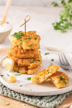 A stack of golden cod fritters on a textured plate with fresh parsley, lemon, and a fork, offering a savory Mediterranean-style seafood appetizer snack