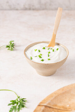 Creamy white yogurt dip in a rustic bowl garnished with fresh green chives and a wooden spoon, perfect as a savory accompaniment for fresh appetizers or snacks in a bright culinary setting
