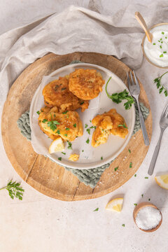 Golden crispy cod fish fritters on a rustic plate served with fresh green parsley lemon and creamy dipping sauce for a tasty Mediterranean snack