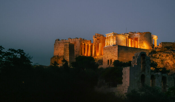 The illuminated Acropolis and Parthenon in Athens, Greece, glow against the evening sky, highlighting one of the world's most iconic ancient landmarks.
