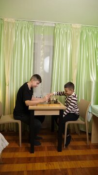 Two brothers are playing chess at a table, taking turns making moves and carefully planning their strategy during the game.