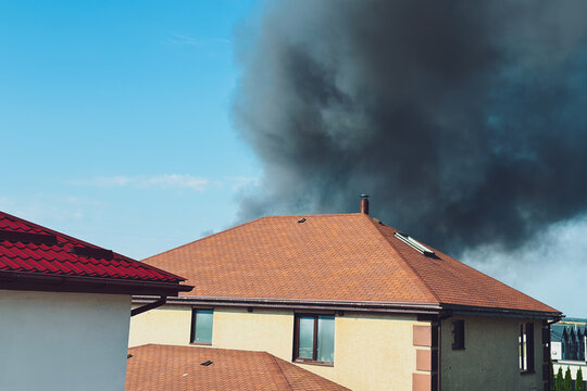 Thick black smoke rises from a fire behind residential homes under a clear sky