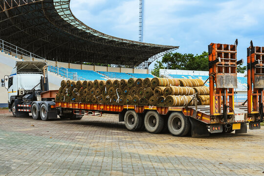 Truck loaded with sod rolls parked at stadium for lawn landscaping and renovation for football field. Large shipment of natural sod rolls on heavy duty truck trailer with stadium bleacher background.