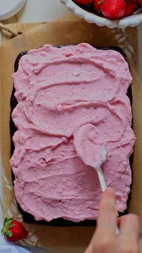 Spreading strawberry cream cheese frosting on chocolate sheet cake. Top view.