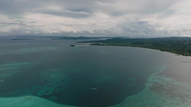 Expansive bay with calm water, green coastal land and distant hills under cloudy sky. Siargao, Philippines.
