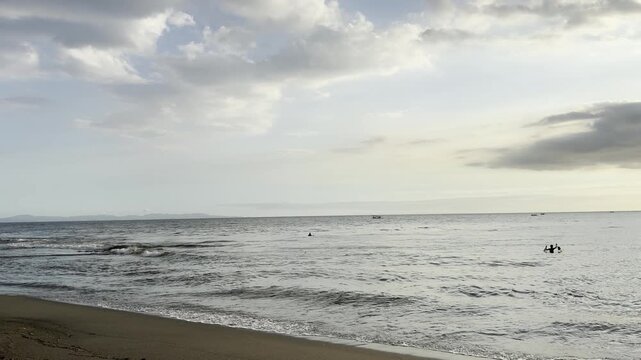 Calm seascape with ocean waves hitting dark sand beach under cloudy sky