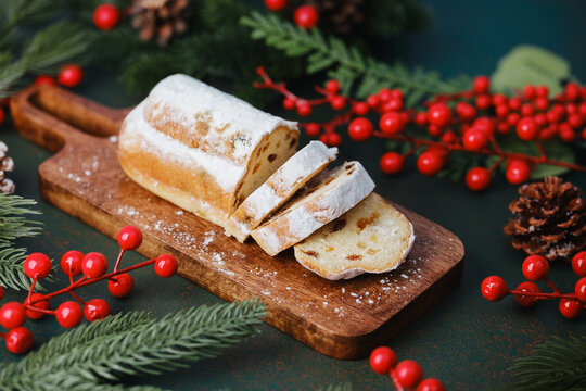Classic Christmas Stollen sliced on wooden board with festive berries and pine cones