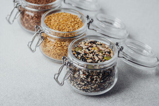 Glass jars filled with different seeds and grains arranged on a light background