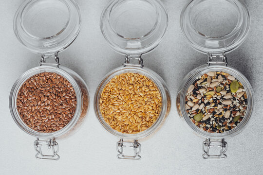 Three glass jars filled with different types of seeds on a light grey background