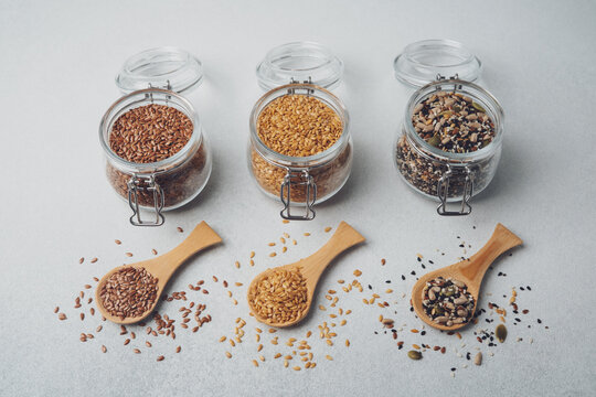 Three glass jars of seeds with wooden spoons on a textured background