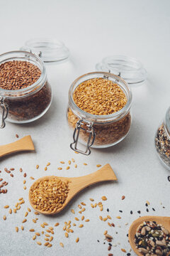 Glass jars and wooden spoons filled with various seeds on a light background