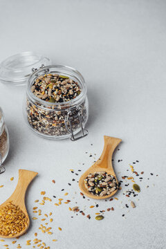 Mixed seeds in a glass jar and wooden spoons on a light background