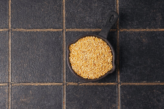 golden flax seeds in a small black pan on a textured dark background