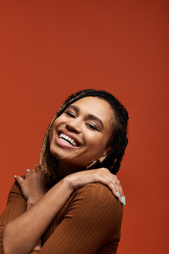 A joyful African American woman models her stylish attire in a vibrant orange setting.