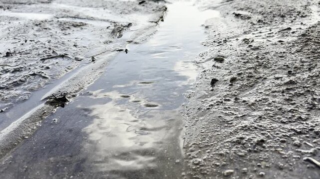Water flowing through muddy ground with sky reflections