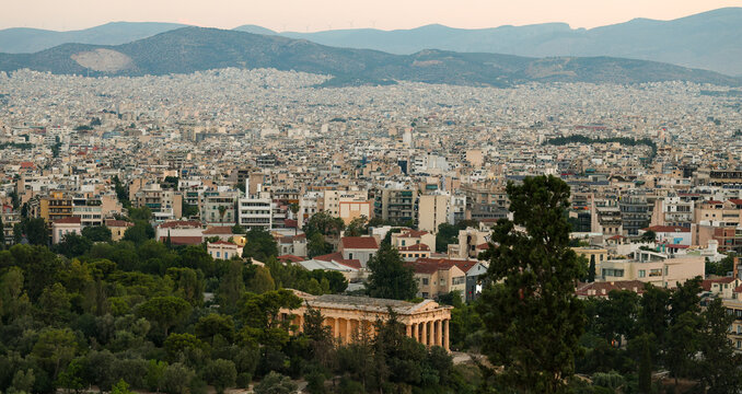 Panoramic view of Athens, Greece, with the Temple of Hephaestus in the foreground and the city stretching to distant mountains under soft evening light.