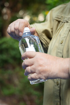 Asian senior woman opening drinking water bottle in green park in the evening, hand closeup shot, concept image for staying hydrated and healthy outdoors