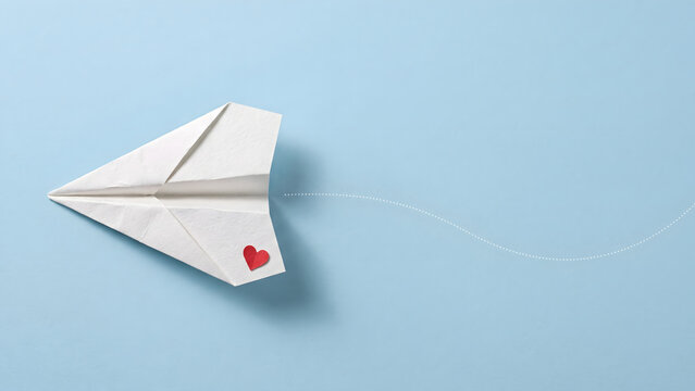 White paper airplane with red heart symbol flying on blue background for love message concept