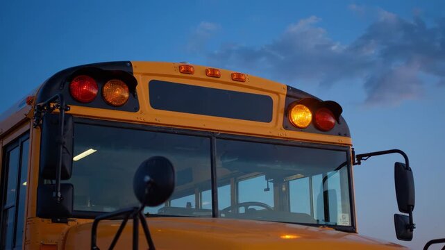 Yellow School Bus Front View With Flashing Lights Against Blue Sky.