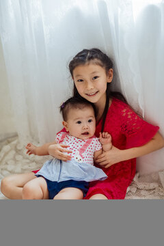 An Asian girl playing indoors with her baby.