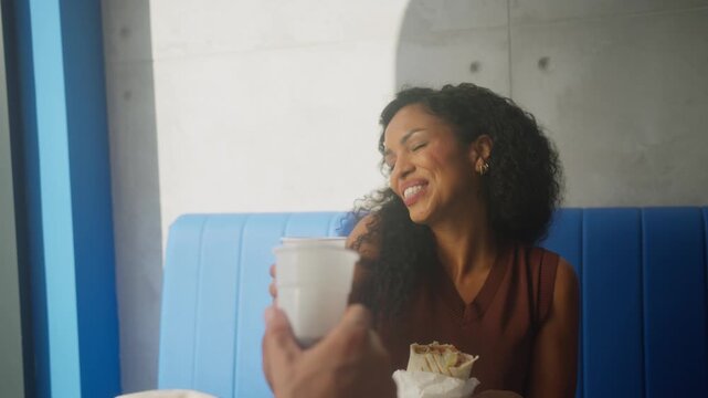 Diverse couple enjoying tasty tortillas, drinks and conversation at fast food restaurant