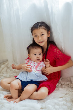 An Asian girl playing indoors with her baby.
