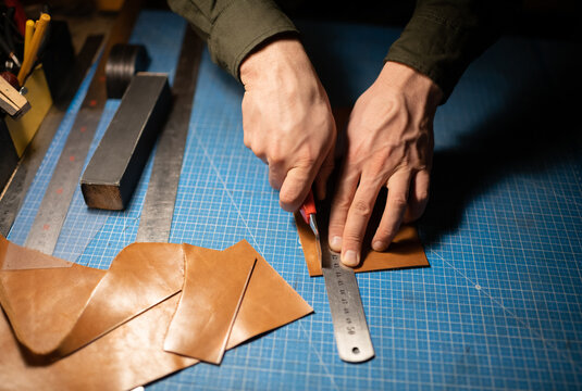 Cropped artisan cutting leather on table