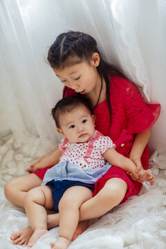 An Asian girl playing indoors with her baby.