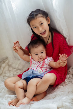An Asian girl playing indoors with her baby.