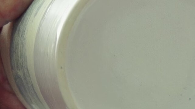 A skilled artisan's hands carefully apply white glaze to a unique striped ceramic bowl. Each gentle brushstroke adds another layer of artistic beauty in a bright studio.