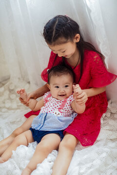 An Asian girl playing indoors with her baby.